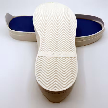 Patchwork Kicks close-up of a white sole with a herringbone tread pattern and the brand name 'pashwork' embossed on it, with a blue footbed visible in the background.