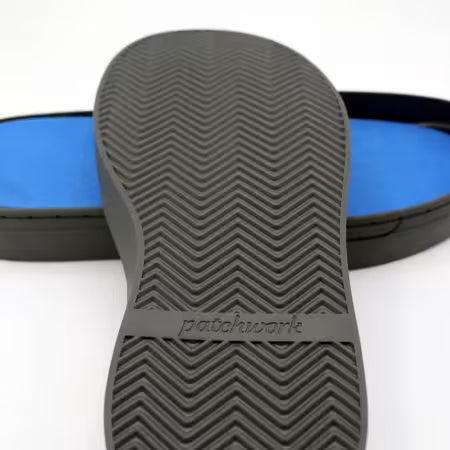Patchwork Kicks close-up of a dark gray sole with a herringbone tread pattern and the brand name 'pashwork' embossed on it, with a blue footbed visible in the background.